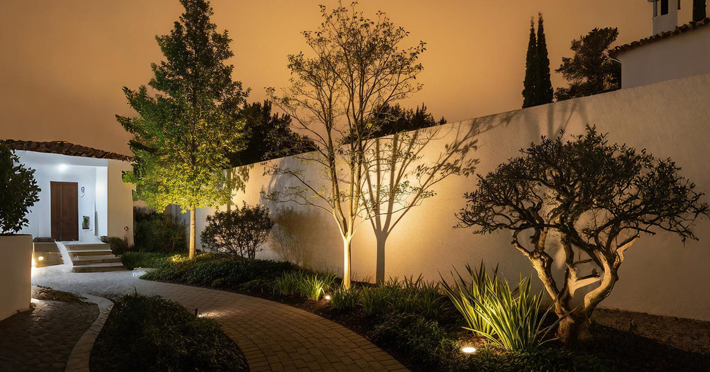 Garden scene with well lights installed flush in lawn beds, uplighting trees, shrubs, and borders for night clarity.
